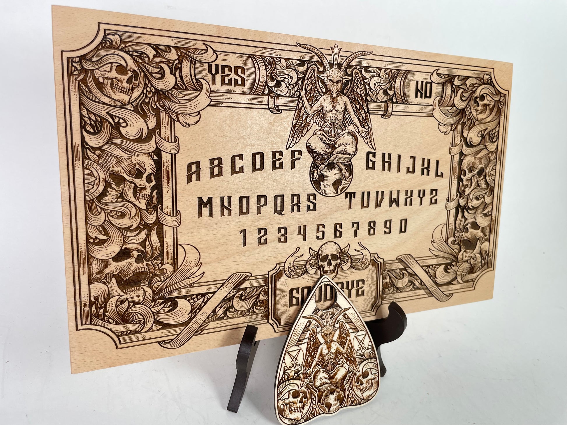 Handcrafted wooden Ouija board with Baphomet imagery, alphabet and number layout, designed as a divination tool and occult altar centerpiece, photographed from top view

