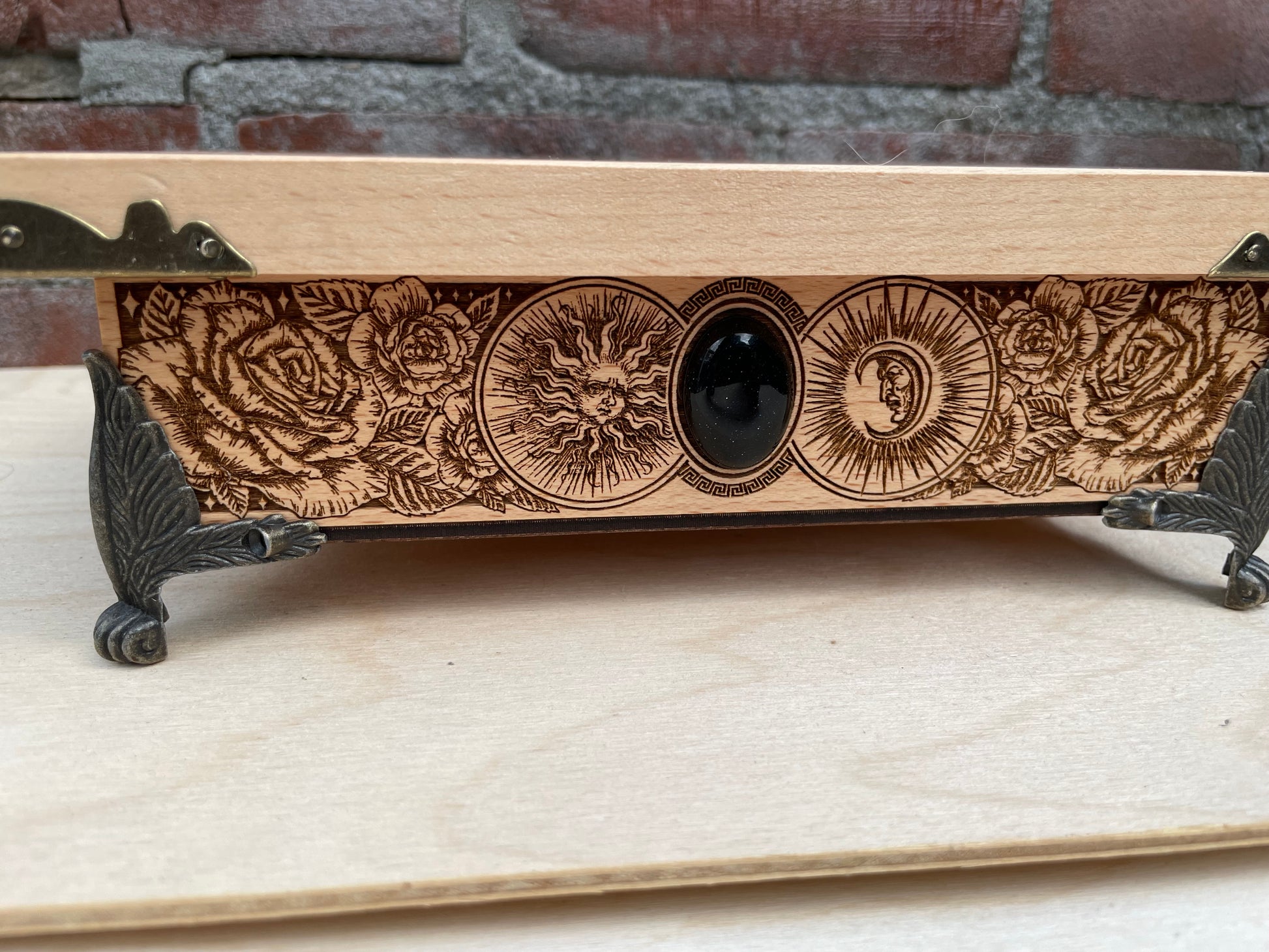 Wooden box with engraved designs on a stand against a brick wall background
