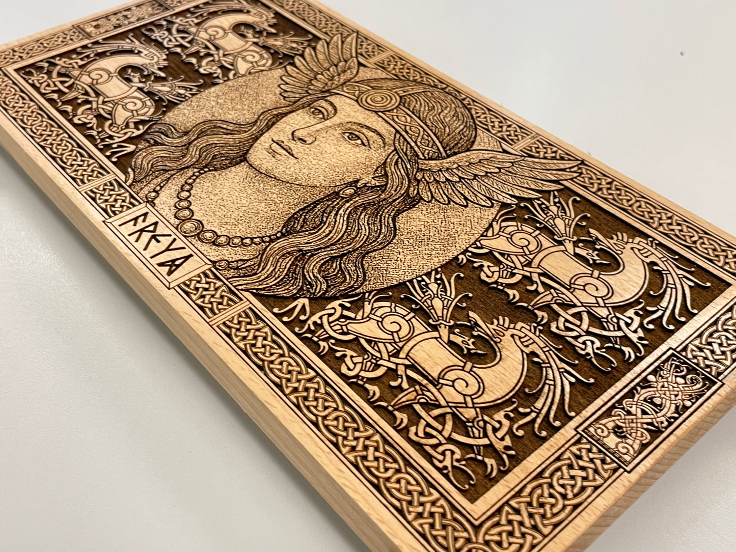 Wooden block with intricate carvings of Freya and decorative Viking patterns on a light gray background