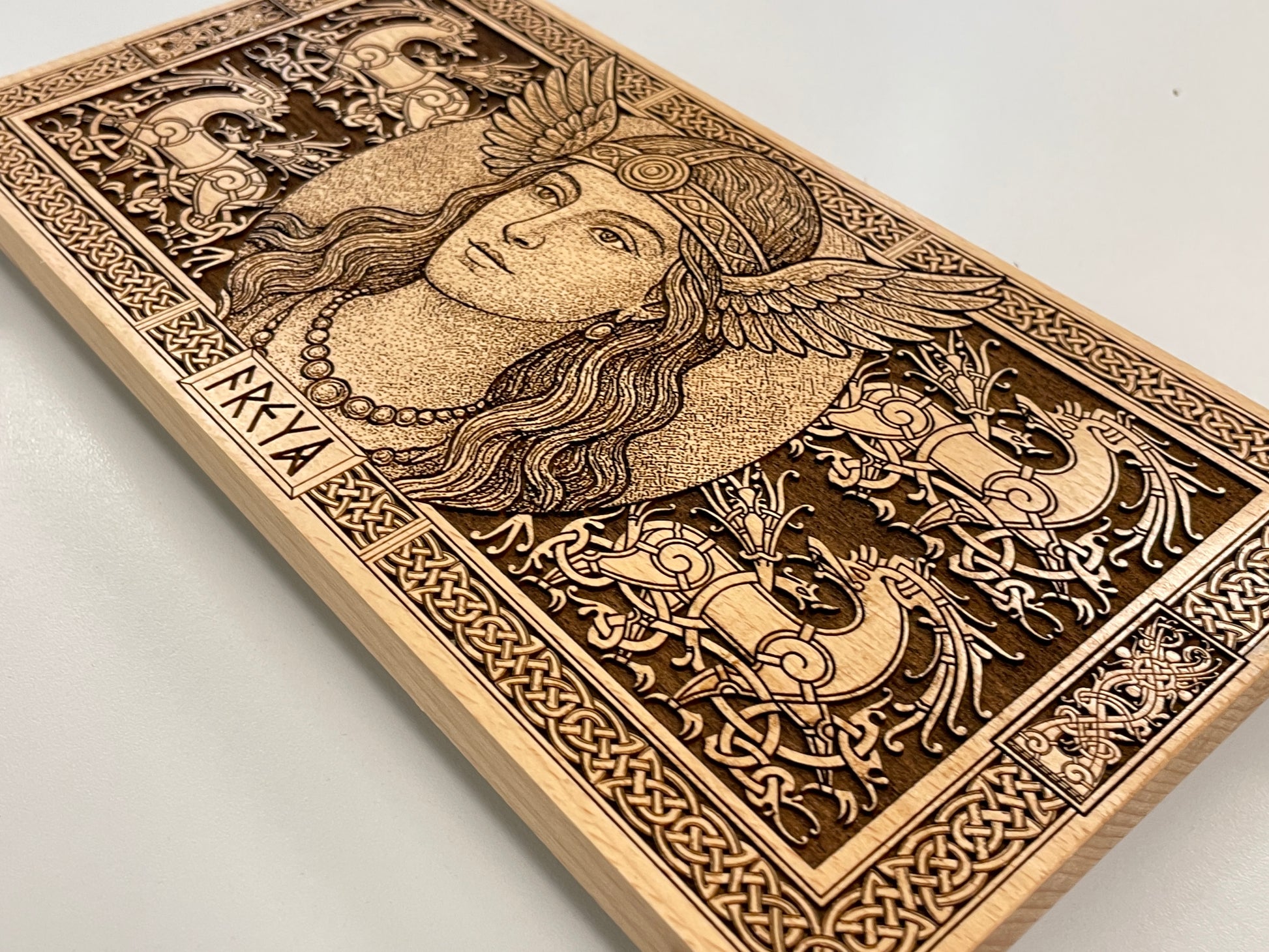 Wooden block with intricate carvings of Freya and decorative Viking patterns on a light gray background