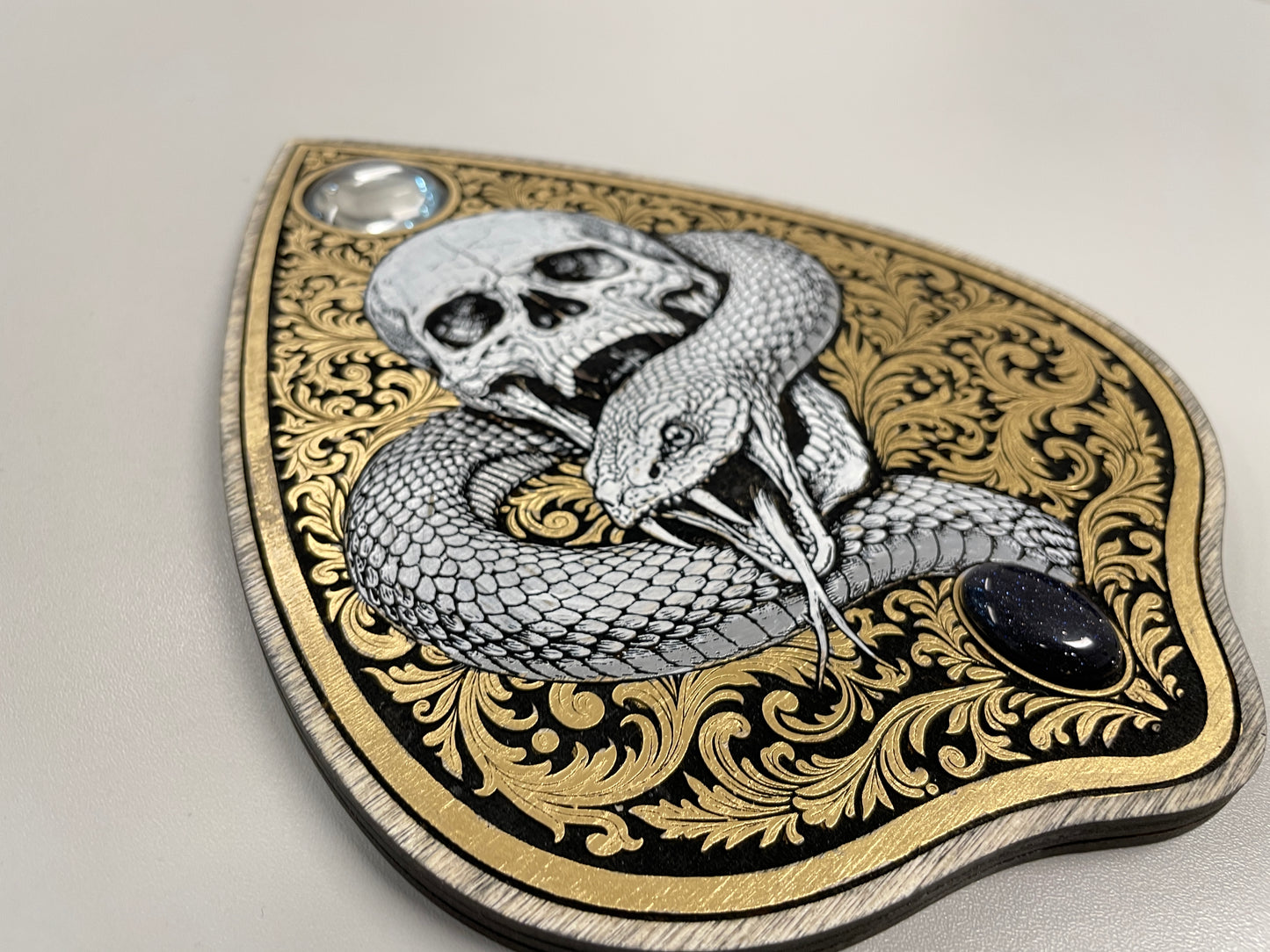 Decorative ouija board planchette with snake and skull design on an ornate shield-shaped background